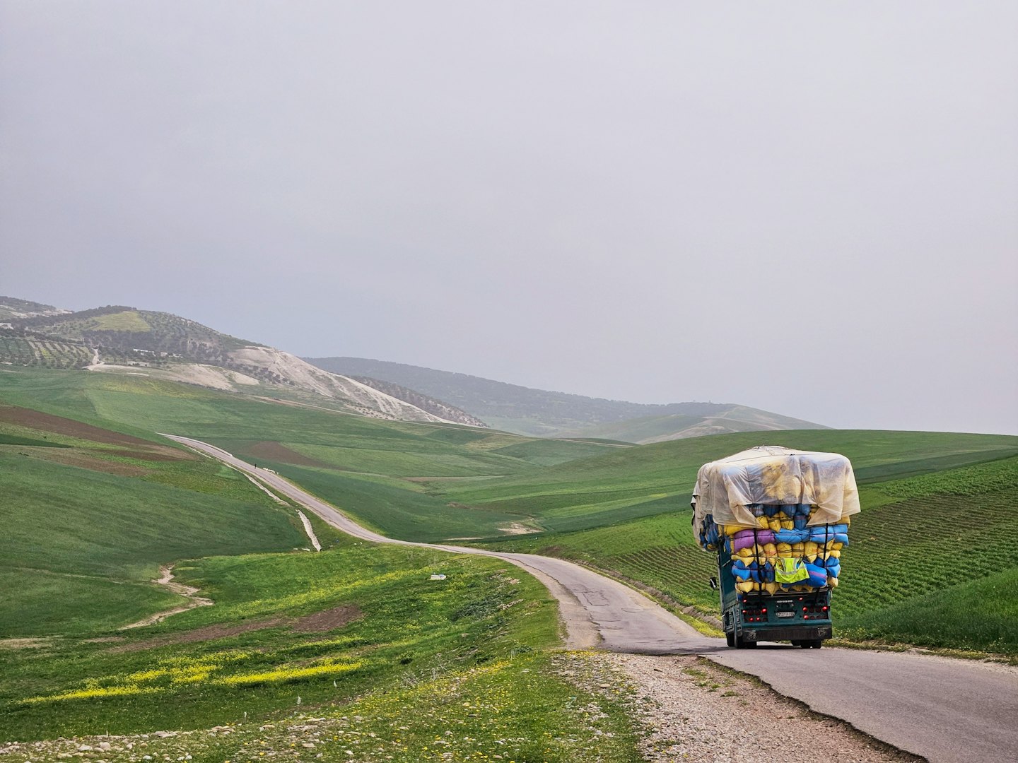 An overloaded cargo truck drives along a winding rural road.