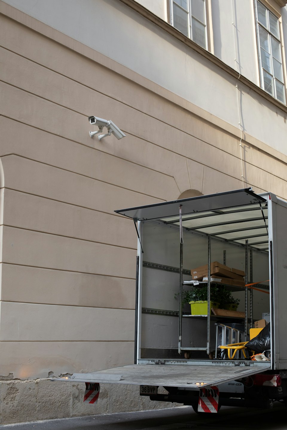 Delivery truck with open ramp parked against a beige building.