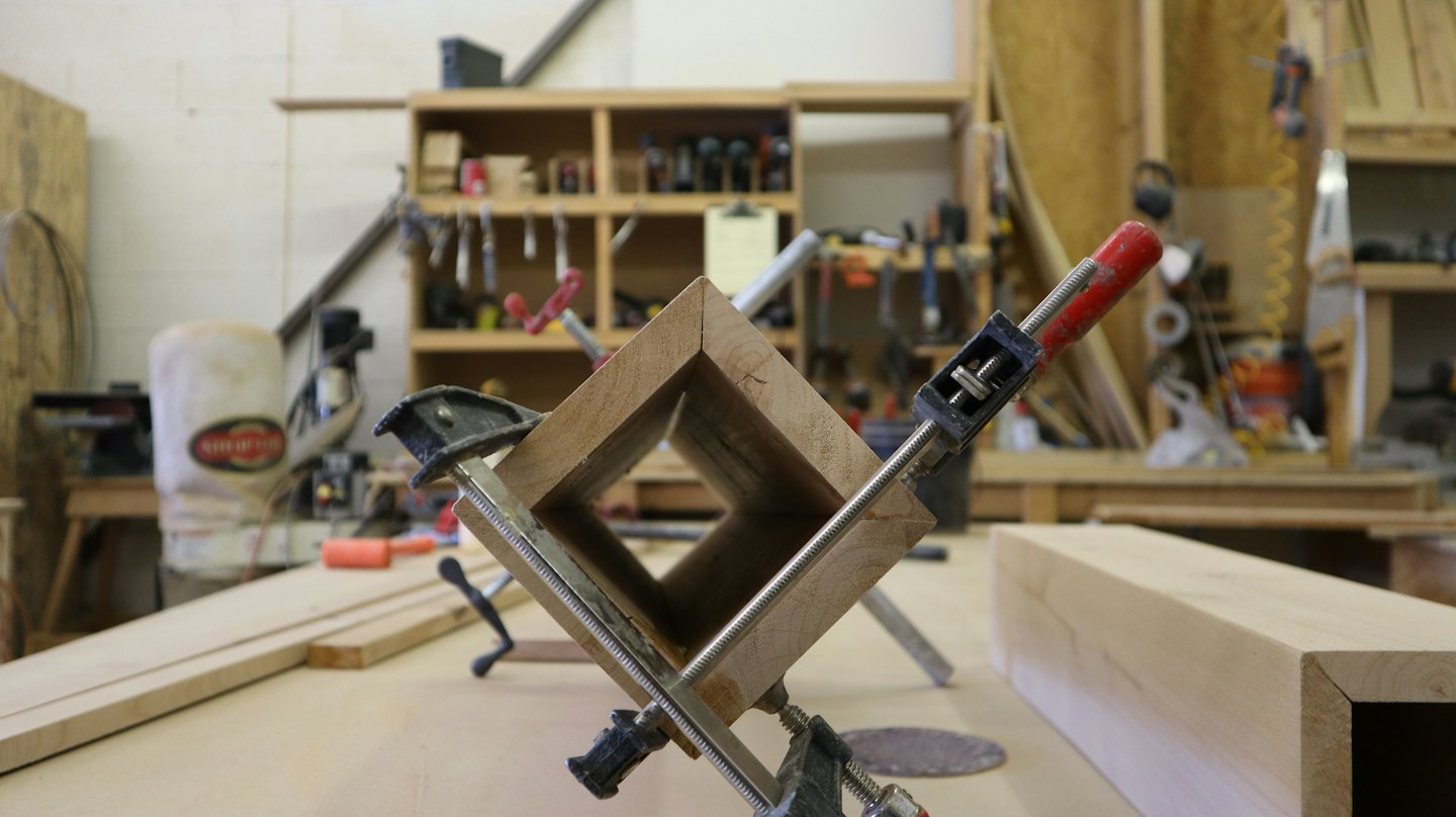 Two F-clamps and one corner clamp hold wood pieces together.