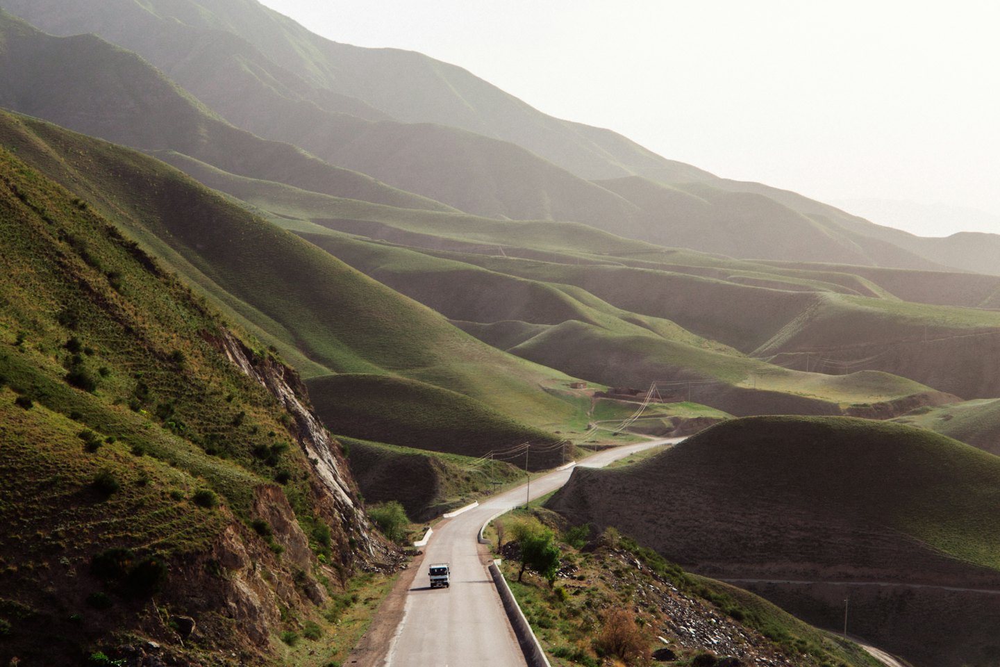 A white truck drives along a winding road through rolling hills.