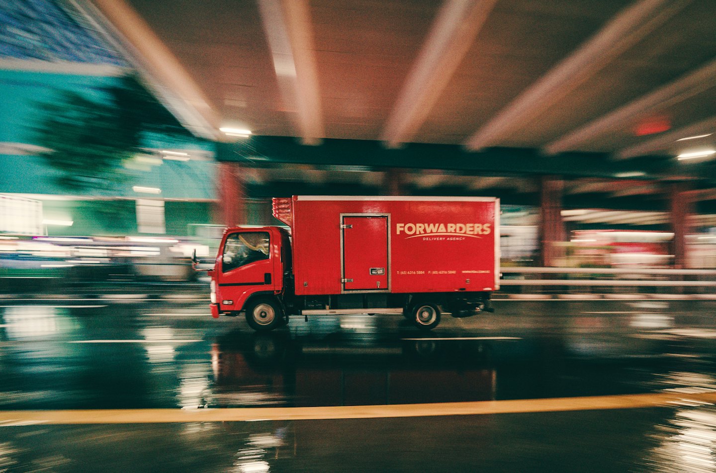 A red delivery truck driving on a wet city street.